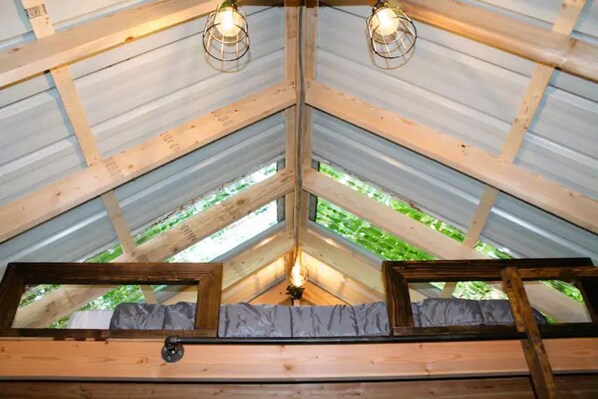 A room with a sloped ceiling, wooden beams, and two windows with curtains.