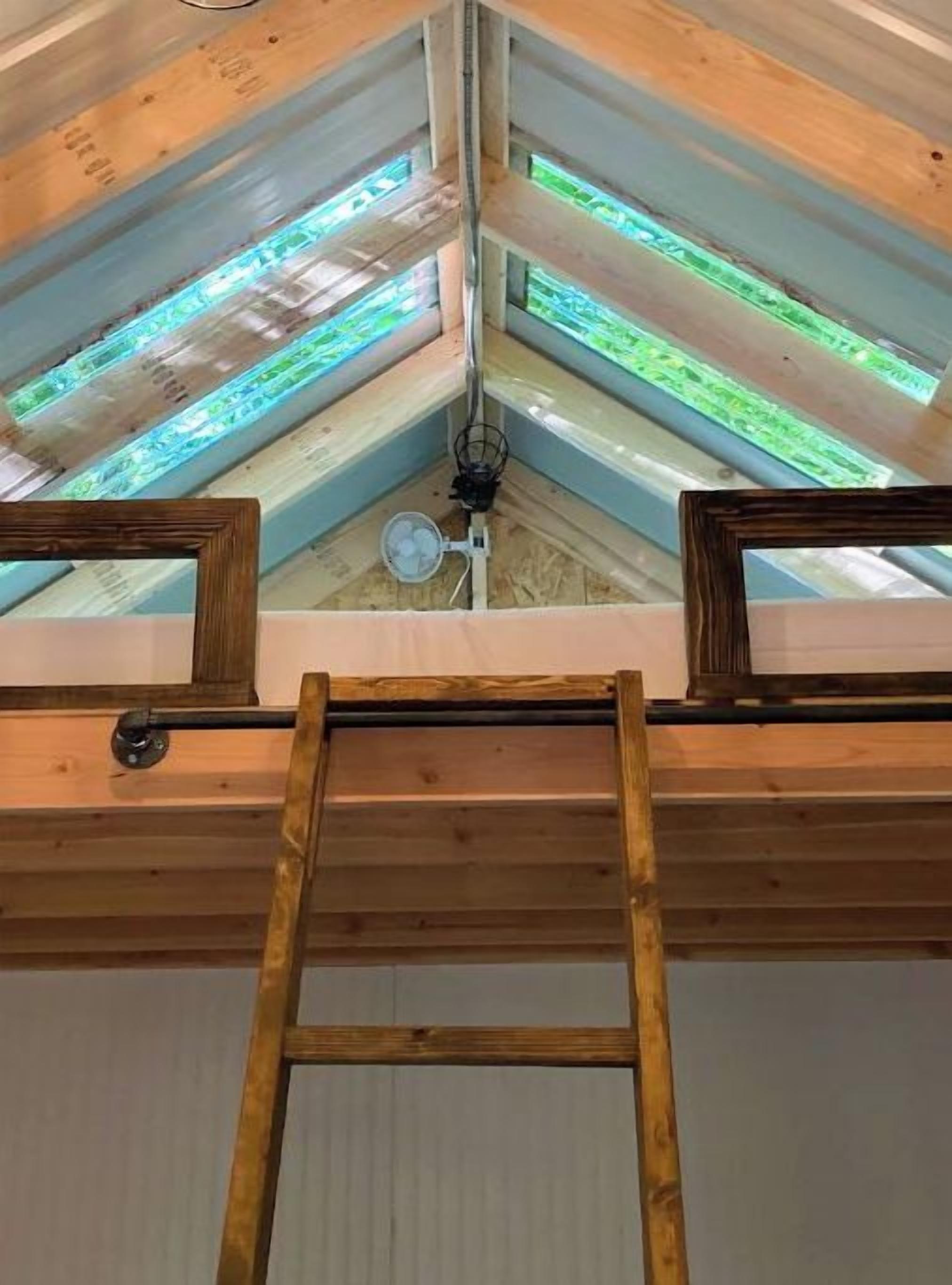 Un tragaluz con una escalera de madera que conduce a un ventilador de techo.