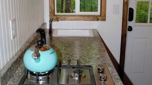 Een keuken met een gasfornuis, een waterkoker en een raam met uitzicht op groen.