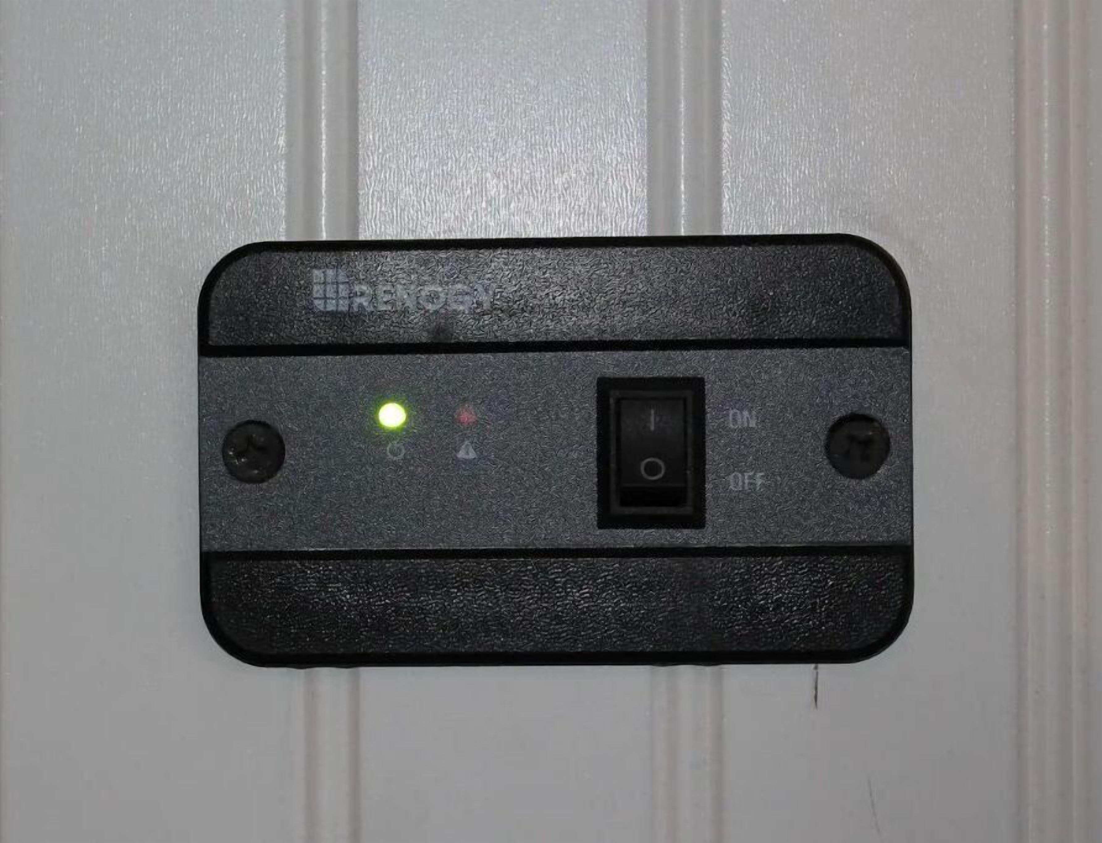 En sort kontrolpanel med en tænd/sluk-kontakt, et grønt lys og to knapper på en hvid dør.