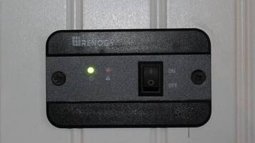 En sort kontrolpanel med en tænd/sluk-kontakt, et grønt lys og to knapper på en hvid dør.