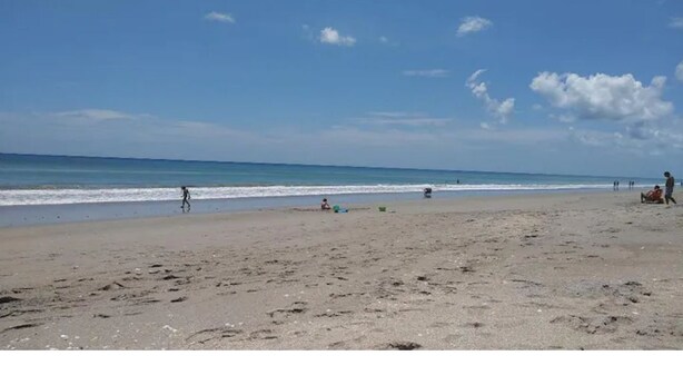 A beach with people walking and playing, and a clear sky.