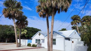 A white building with a blue roof, surrounded by palm trees.