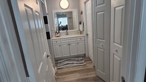 A hallway with wooden flooring, white doors, and a round mirror above a sink.