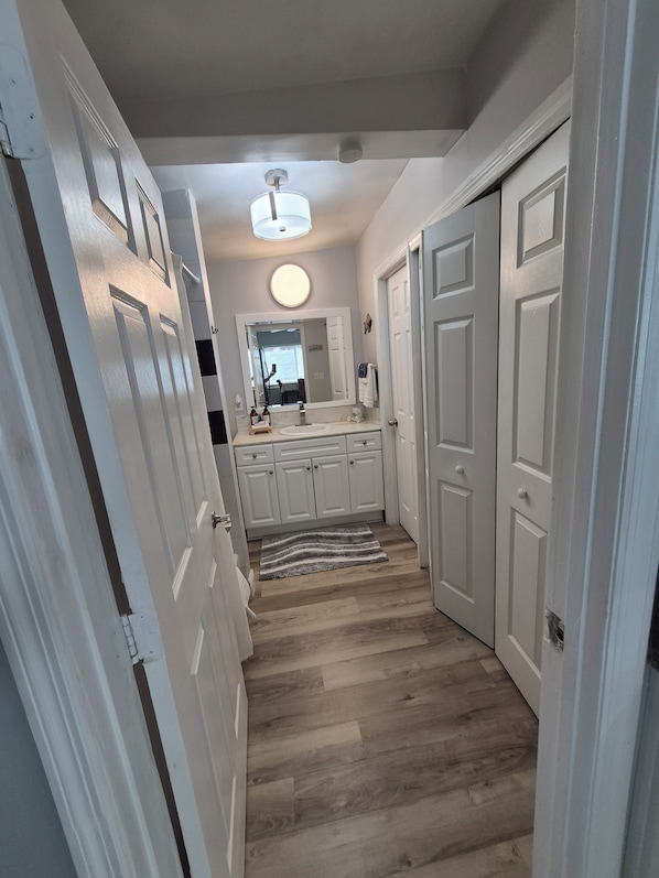 A hallway with wooden flooring, white doors, and a round mirror above a sink.
