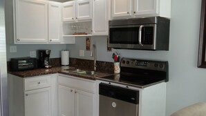 A modern kitchen with white cabinets, a built-in microwave, a dishwasher, and a ceiling fan.