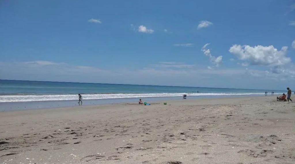 Una playa con gente caminando y jugando, bajo un cielo despejado.