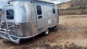 A silver trailer with the brand name "AIRSTREAM" on the back, parked on a dirt ground with a rocky hill in the background. - Zion's Cozy Airstream #2 (Apple Valley)