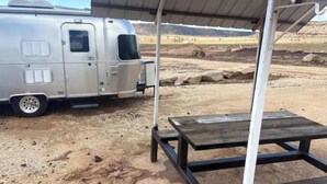 A silver RV parked under a covered area with a metal table and bench. - Zion's Cozy Airstream #2 (Apple Valley)
