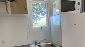 A compact kitchen with a black countertop, a white refrigerator, a microwave, a sink, and a window with a view of trees.