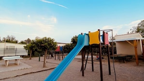 A playground with a blue slide, benches, and a fenced area.