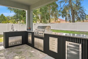 Una cocina al aire libre con parrilla, pileta y alacenas.