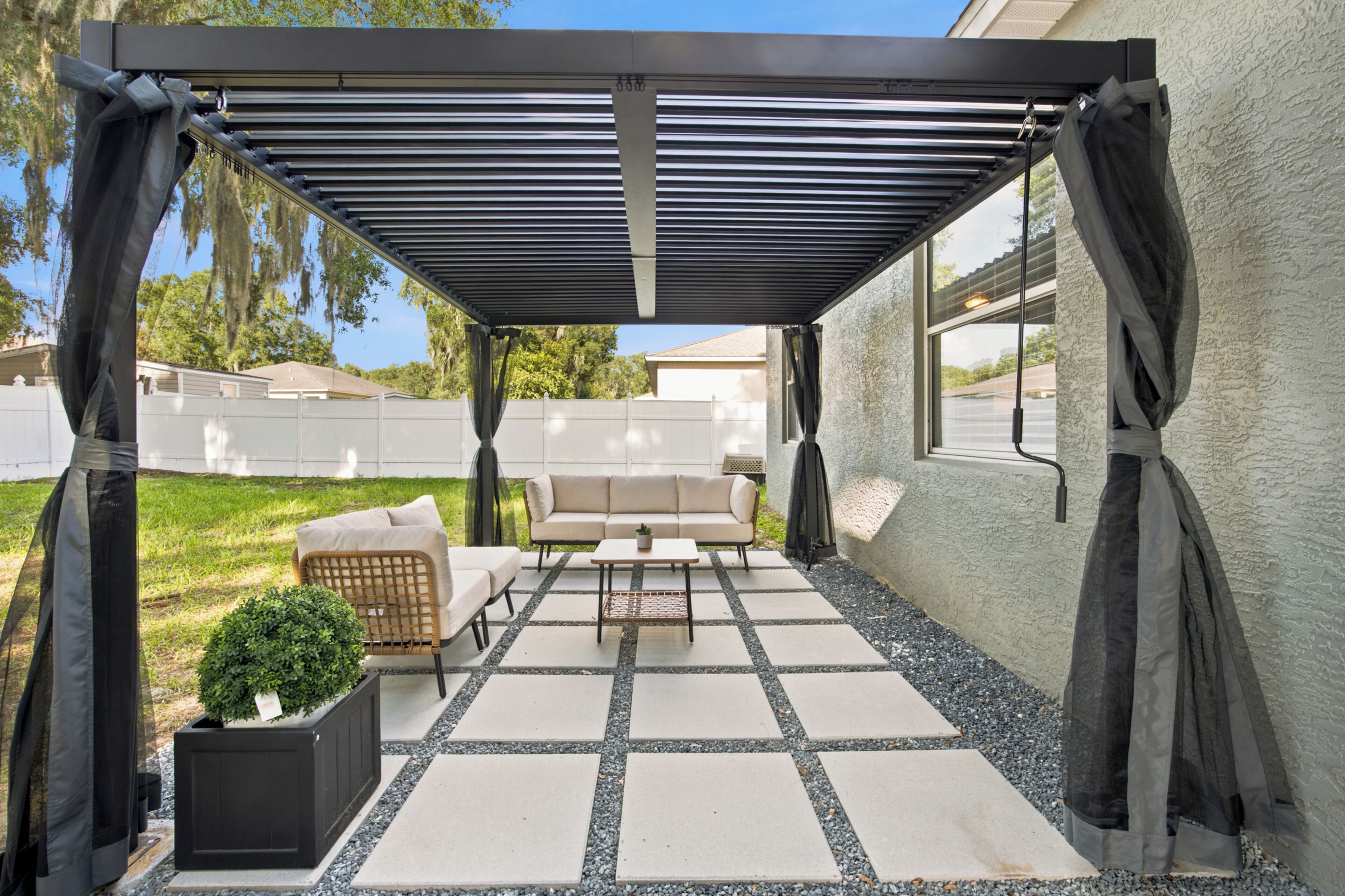 A covered patio area with a pergola, outdoor furniture, and a potted plant.