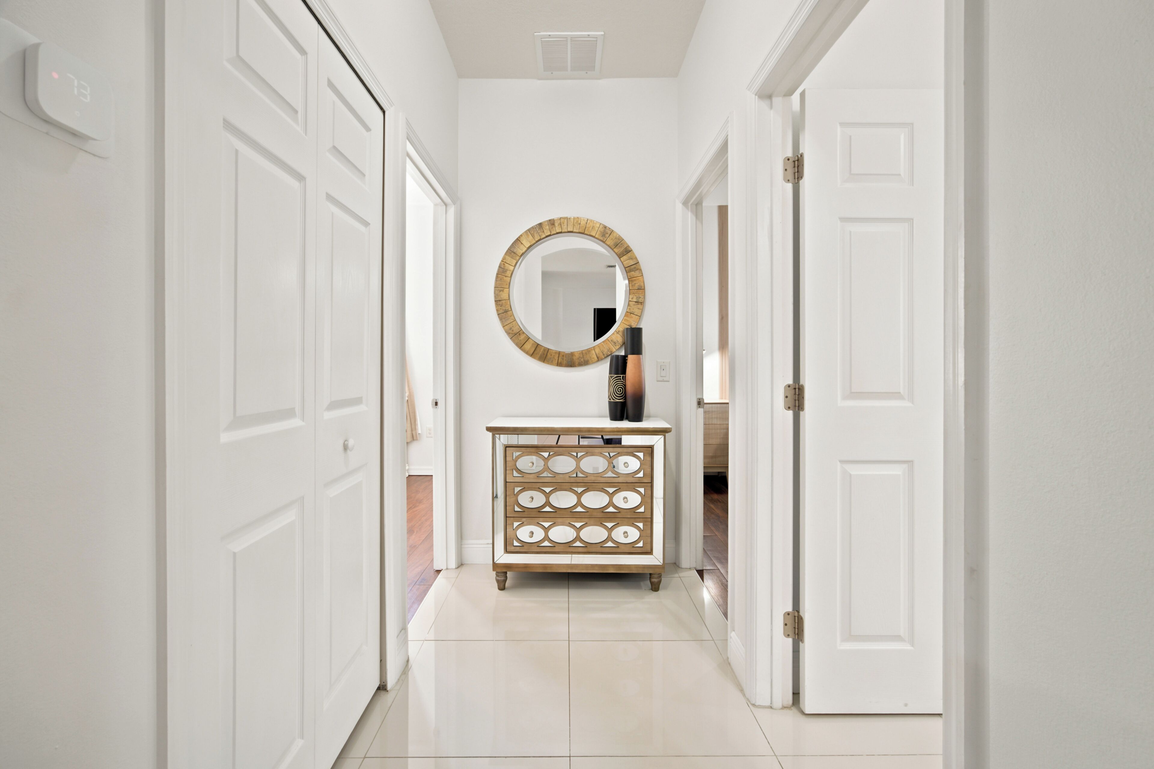 A hallway with white doors, a round mirror, and a wooden dresser with drawers.