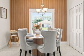 Een eetkamer met een ronde tafel, vier stoelen, een vaas met bloemen en een kroonluchter.