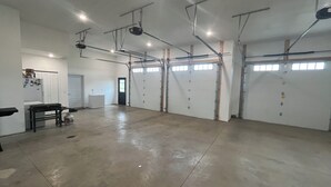 Et rummeligt indendørs område med betongulv, flere garageporte og loftmonterede lysarmaturer.