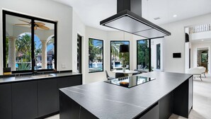 A modern kitchen with a large island, black cabinetry, and large windows offering views of a pool and palm trees. - WATERFRONT MANSION (Fort Lauderdale)