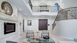 A spacious living area with a fireplace, a glass coffee table, and a high ceiling with a balcony. - WATERFRONT MANSION (Fort Lauderdale)
