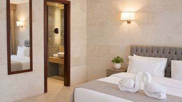 A hotel room with a bed, a nightstand with a lamp, a mirror, and a bathroom visible through an open door.
