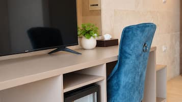Een moderne kantoorruimte met een bureau, een computerscherm, een kleine koelkast, een blauwe stoel, een potplant en een wandlamp.