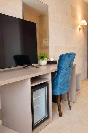 A modern office space with a desk, a computer monitor, a small refrigerator, a blue chair, a potted plant, and a wall-mounted lamp. - Byblos Gate Hotel (Byblos)