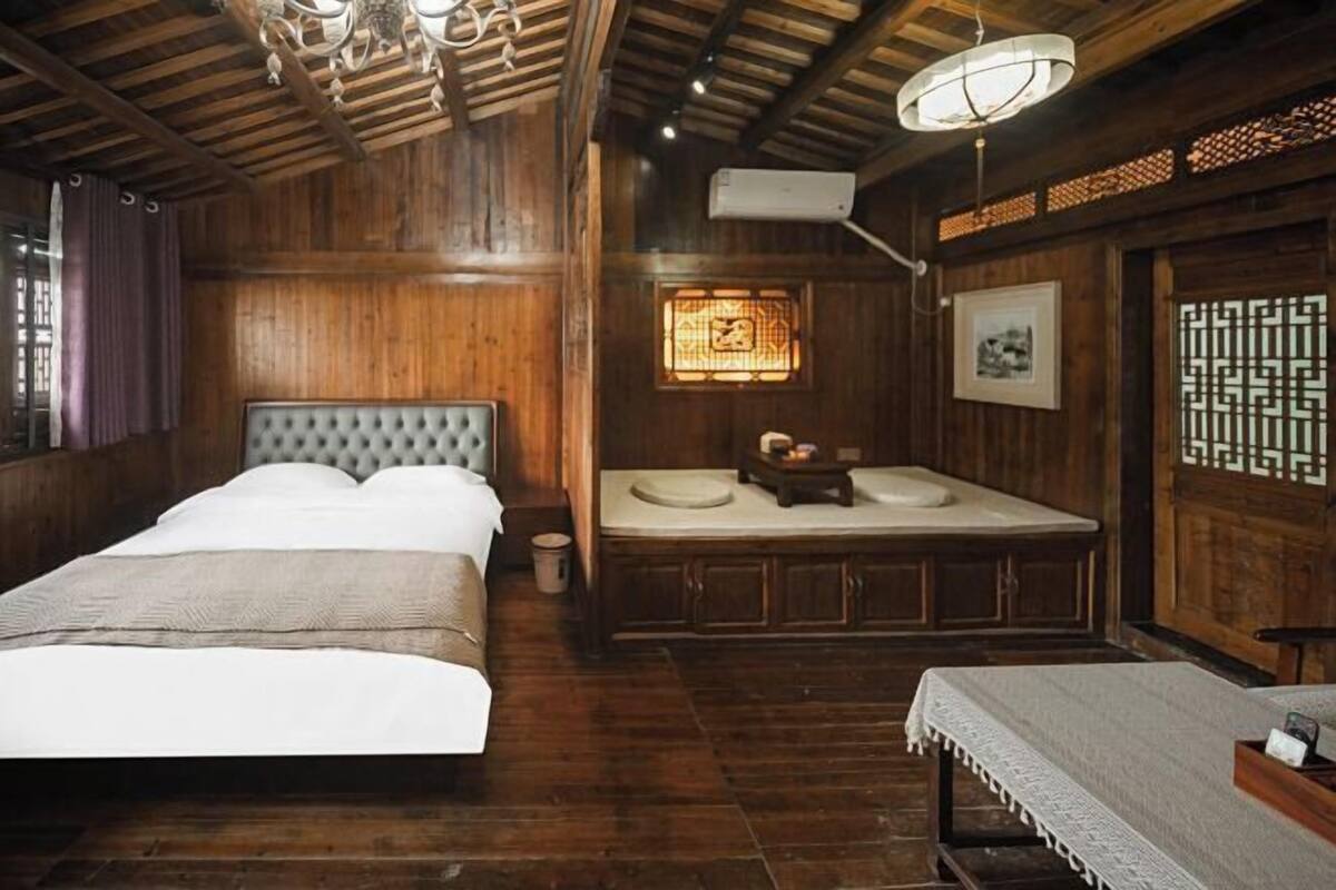 Una habitación tradicional de madera con cama, una mesita y una ventana con celosía decorativa.