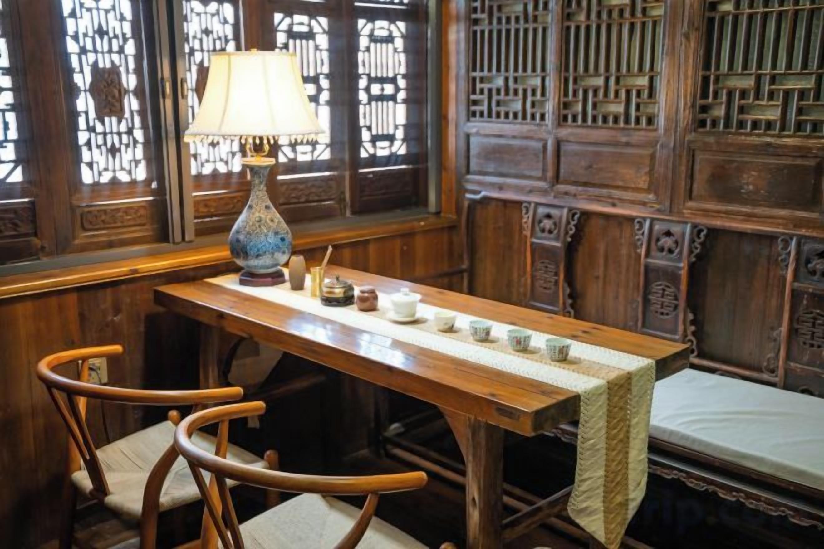 A traditional wooden room with a table set for tea, two chairs, and a window with intricate lattice design.