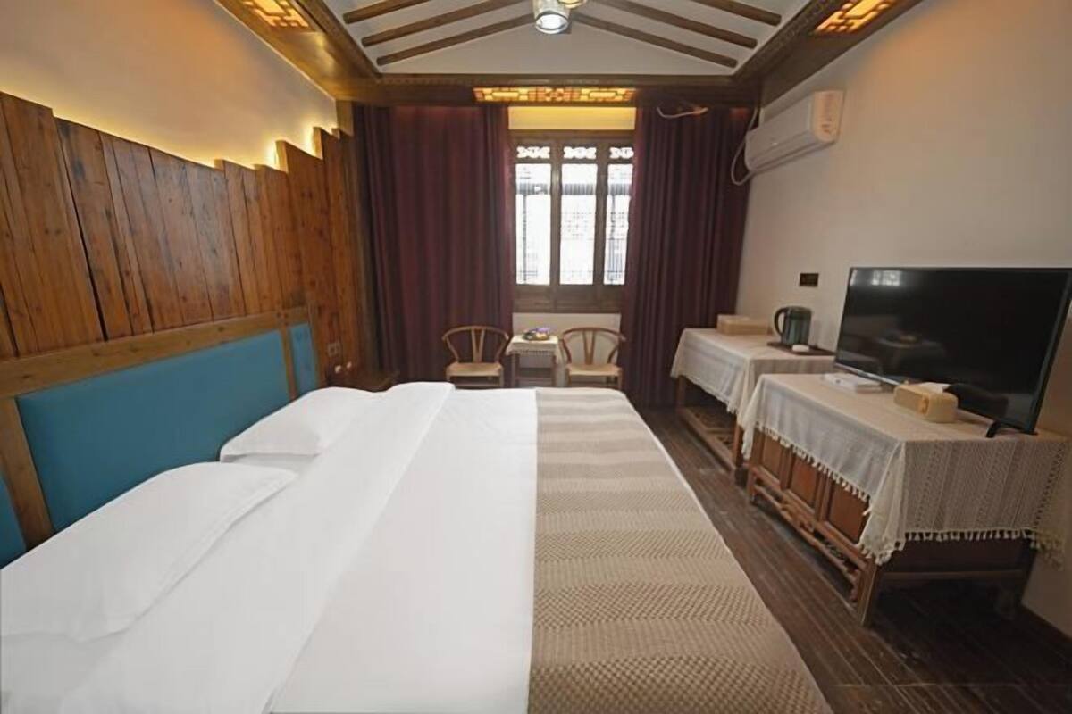 Habitación de hotel con una cama grande, televisor, una mesita con mantel y una ventana con cortinas.