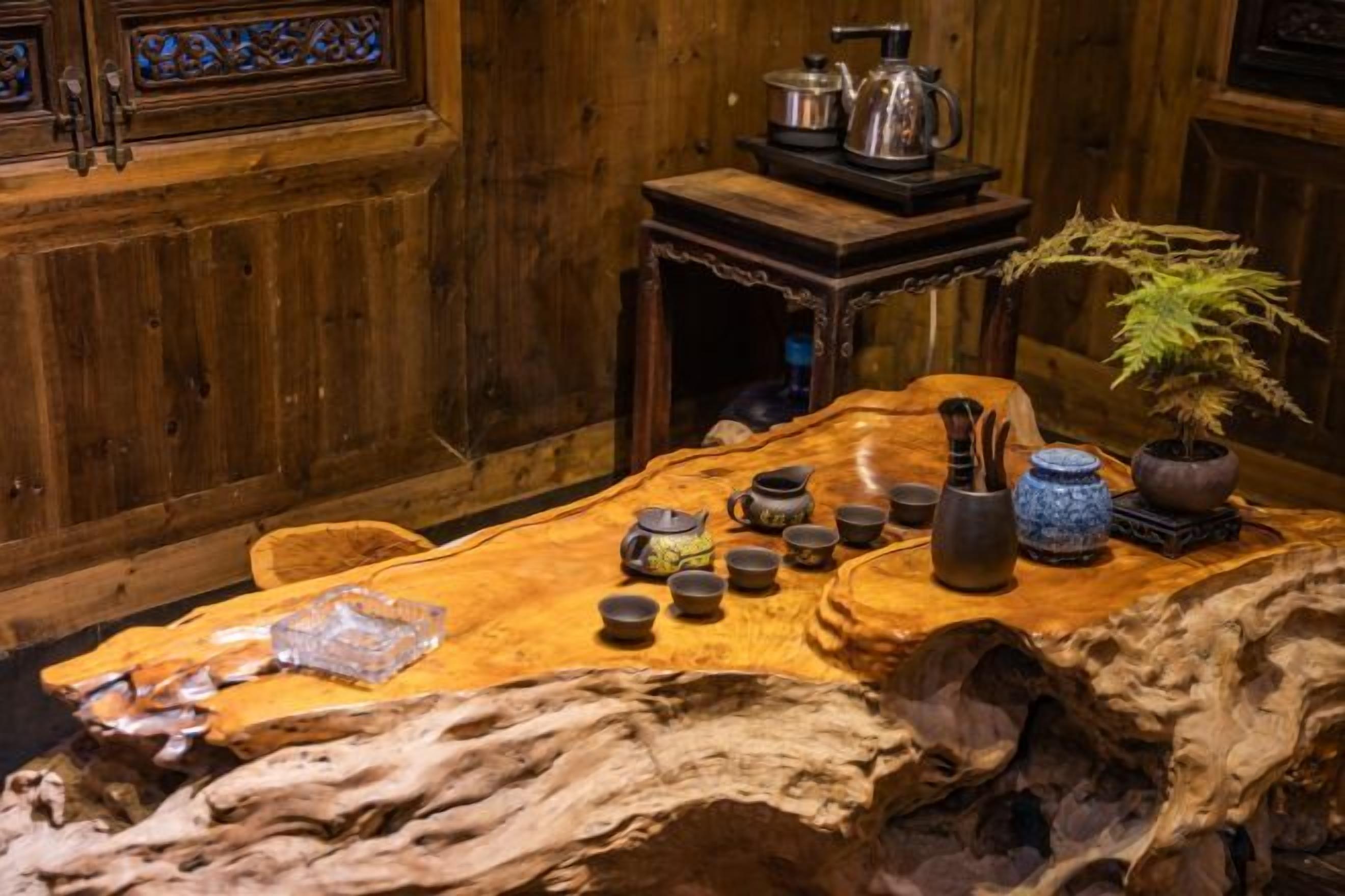 A wooden dining table with various ceramic items, a potted plant, and a rustic wooden chair.