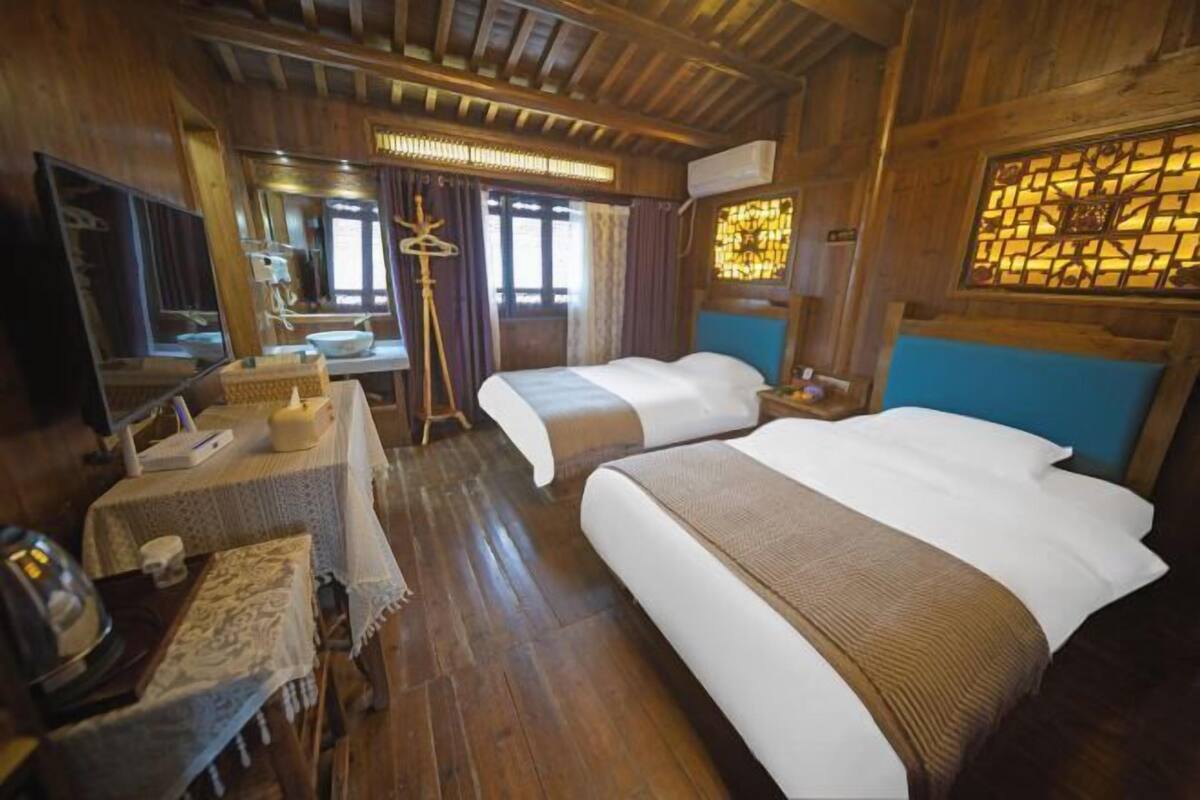 Una habitación de madera con dos camas, un escritorio, un espejo y una ventana con cortinas.