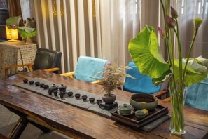 A wooden table with a tea set, a bonsai, and a vase with flowers.