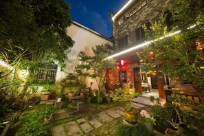 A courtyard with stone pathways, potted plants, and a building with a red-lit entrance. - Building A, Futongyuan Inn, Tianqi Hongcun, Huangshan (Yi County)