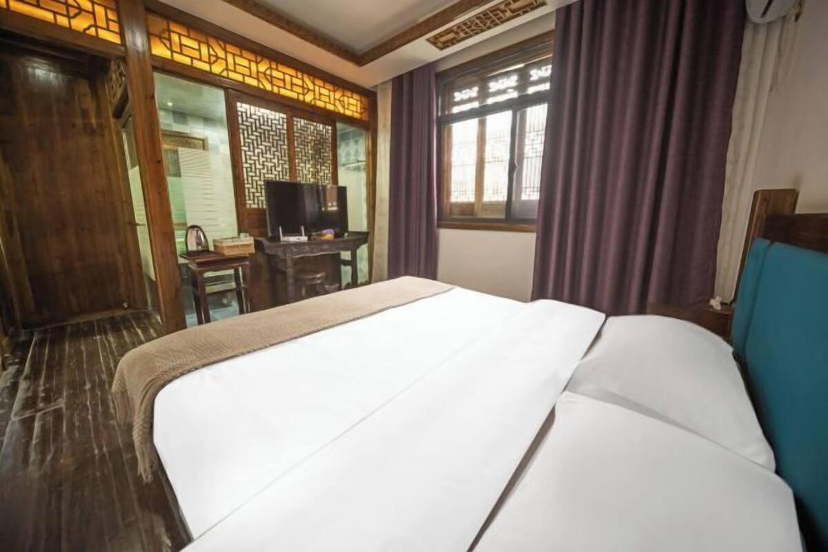 Habitación de hotel con una cama grande, muebles de madera, televisor y ventana con cortinas.