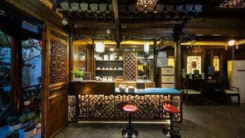A traditional interior with a wooden counter and stools, a tiled floor, and a decorative ceiling.