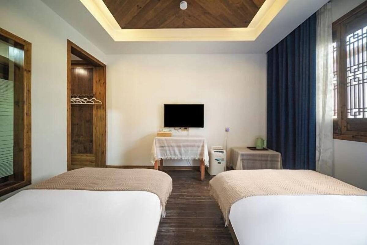 Habitación de hotel con dos camas, televisión, una mesita y una ventana con cortinas.