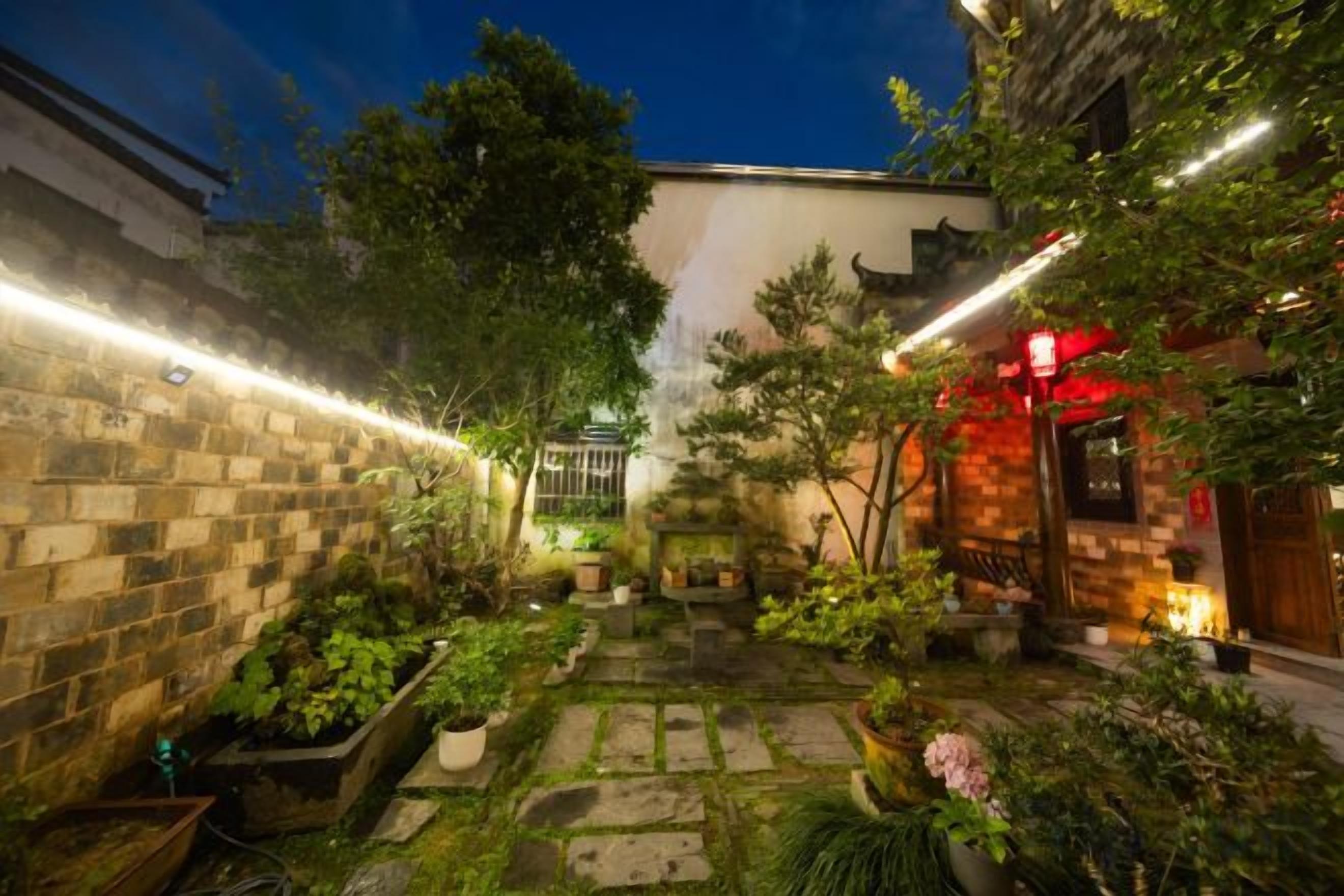 A courtyard with stone pathways, potted plants, and a traditional building with red lanterns.