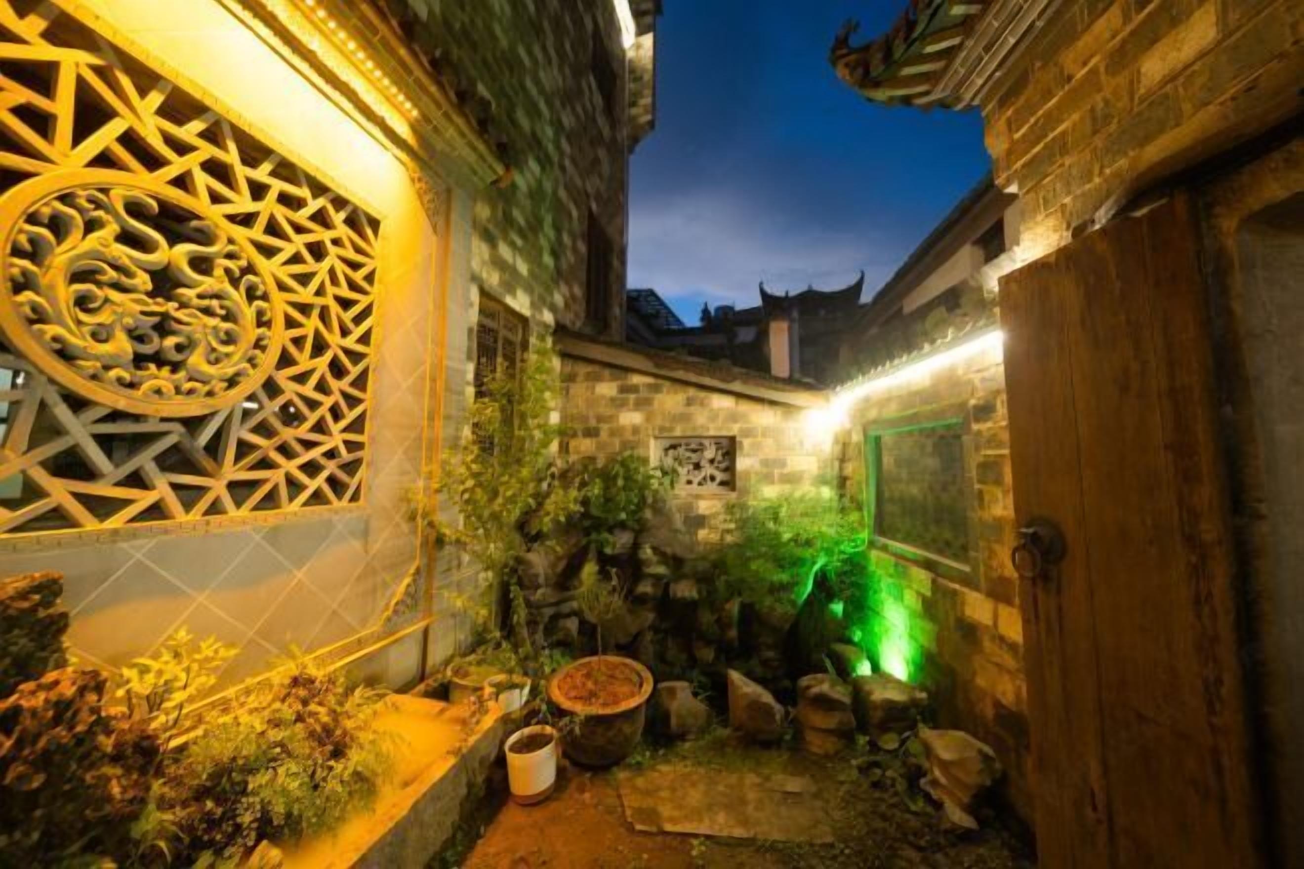 A traditional courtyard with stone walls, a decorative gate, and a small garden area with rocks and plants.