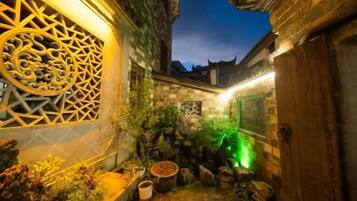 A traditional courtyard with stone walls, a decorative gate, and a small garden area with rocks and plants.