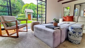 A modern living room with a view of a garden, a wooden door, and a sofa with a book and a plant on it. - Casa Três Rios - Campos do Jordão (Campos do Jordão)