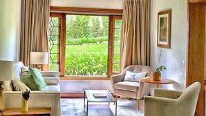 A living room with a sofa, armchair, coffee table, and a view of greenery through large windows. - Casa Três Rios - Campos do Jordão (Campos do Jordão)