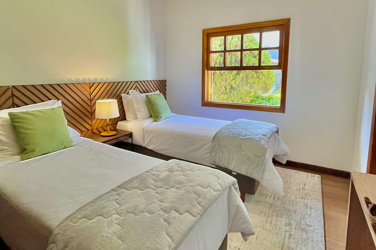 A hotel room with two beds, a window with a view, a ceiling light, and a wooden headboard.