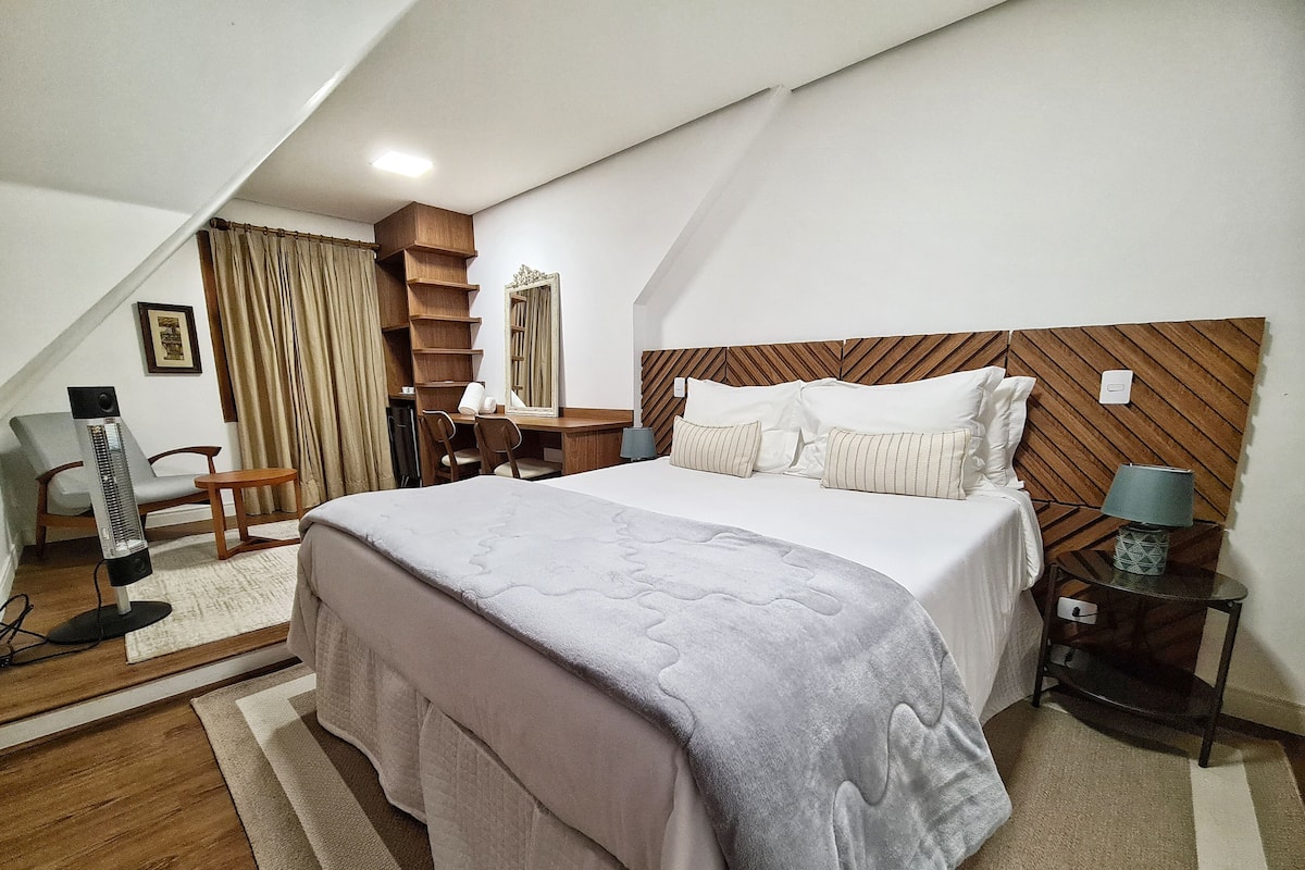 A bedroom with a bed, bedside table, lamp, and a desk with chair.