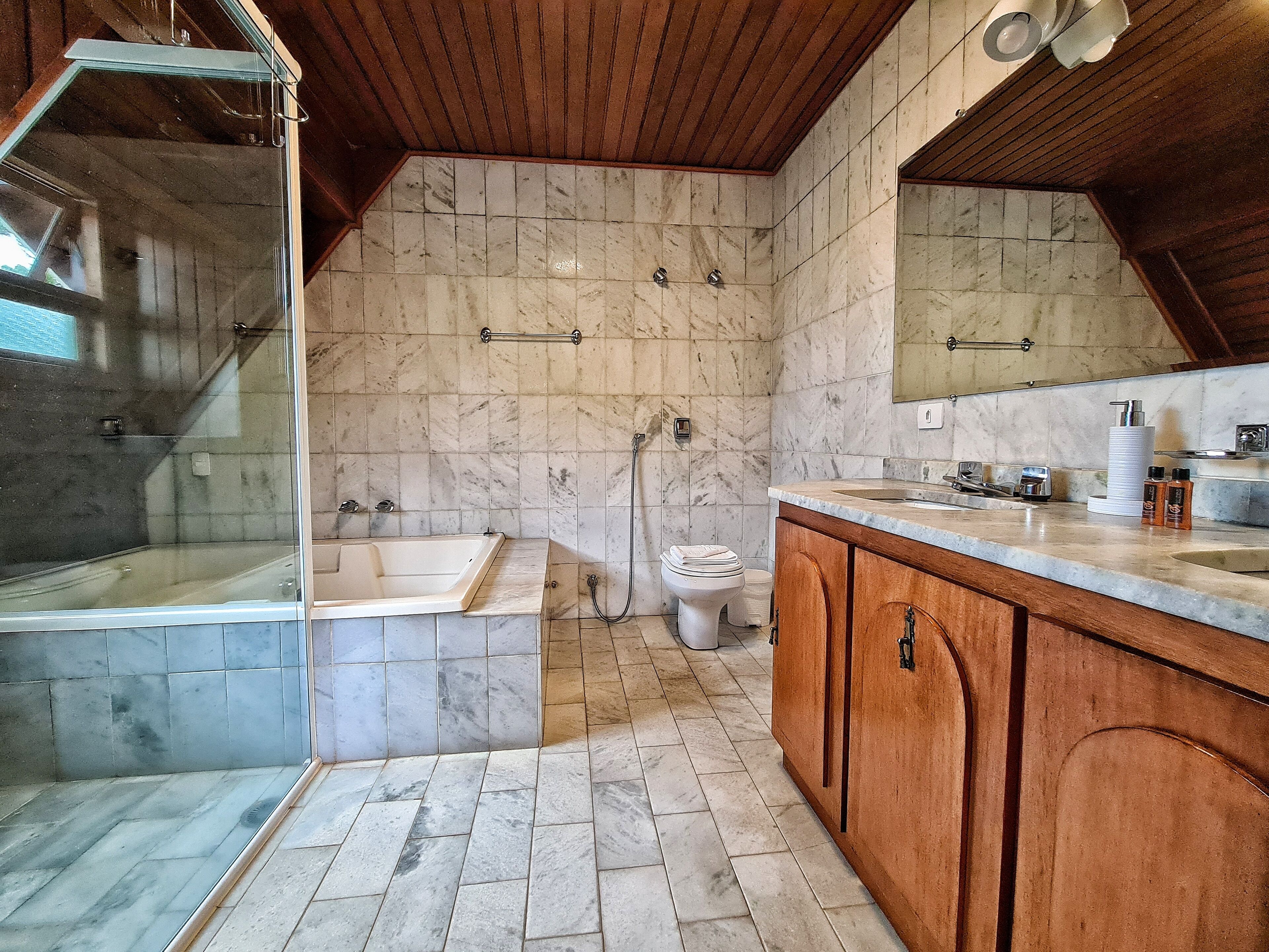 A bathroom with a glass-enclosed shower, a freestanding bathtub, a toilet, and wooden cabinets.