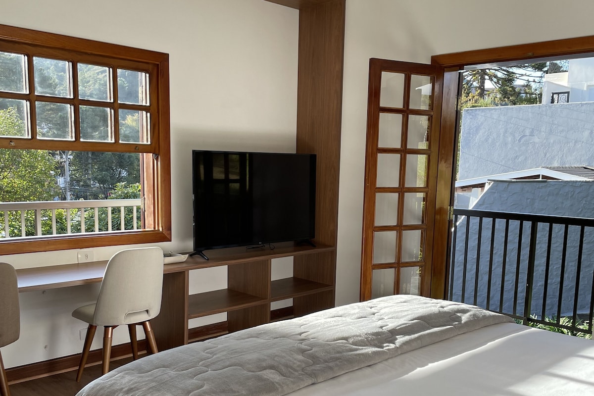 Un dormitorio con cama, escritorio con silla, televisor y balcón con barandilla.