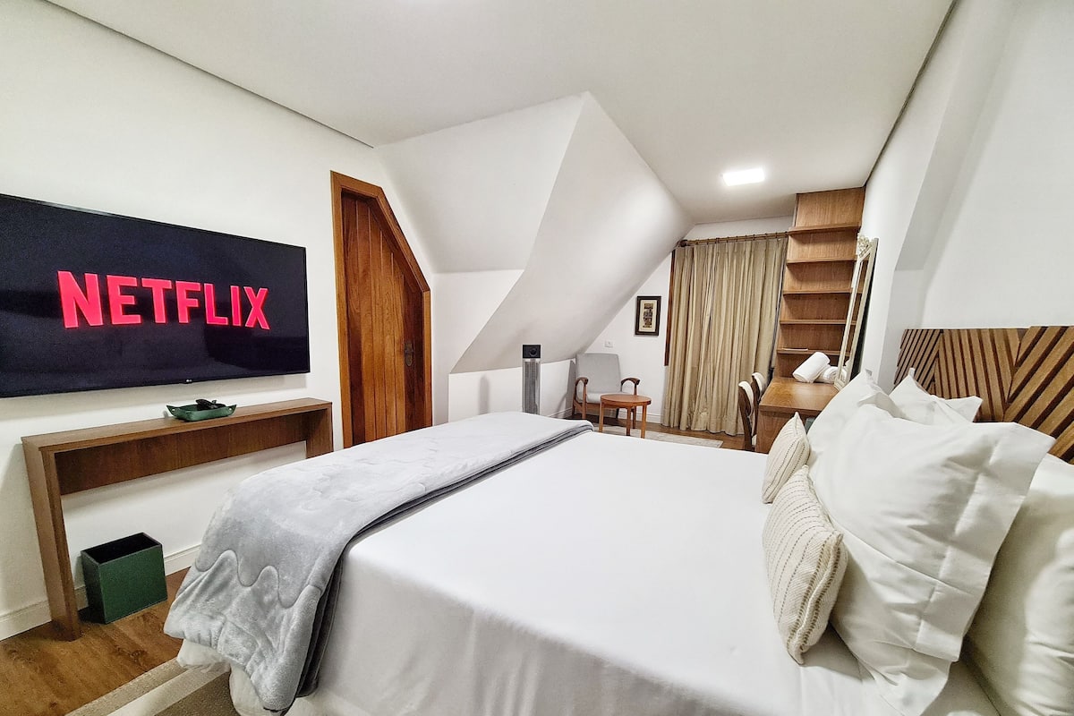 A hotel room with a bed, a TV mounted on the wall, a desk, and a chair.