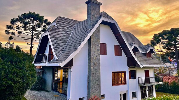 A modern two-story house with a sloped roof, stone facade, and a balcony. - Casa Três Rios - Campos do Jordão (Campos do Jordão)