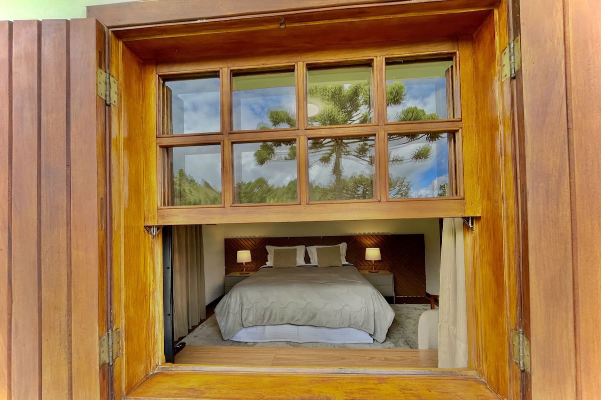 A bedroom with a large window, a bed, and a nightstand.