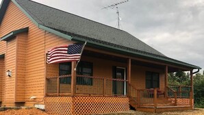 Ett envåningshus byggt av trä, med en veranda, en liten terrass och en amerikansk flagga.
