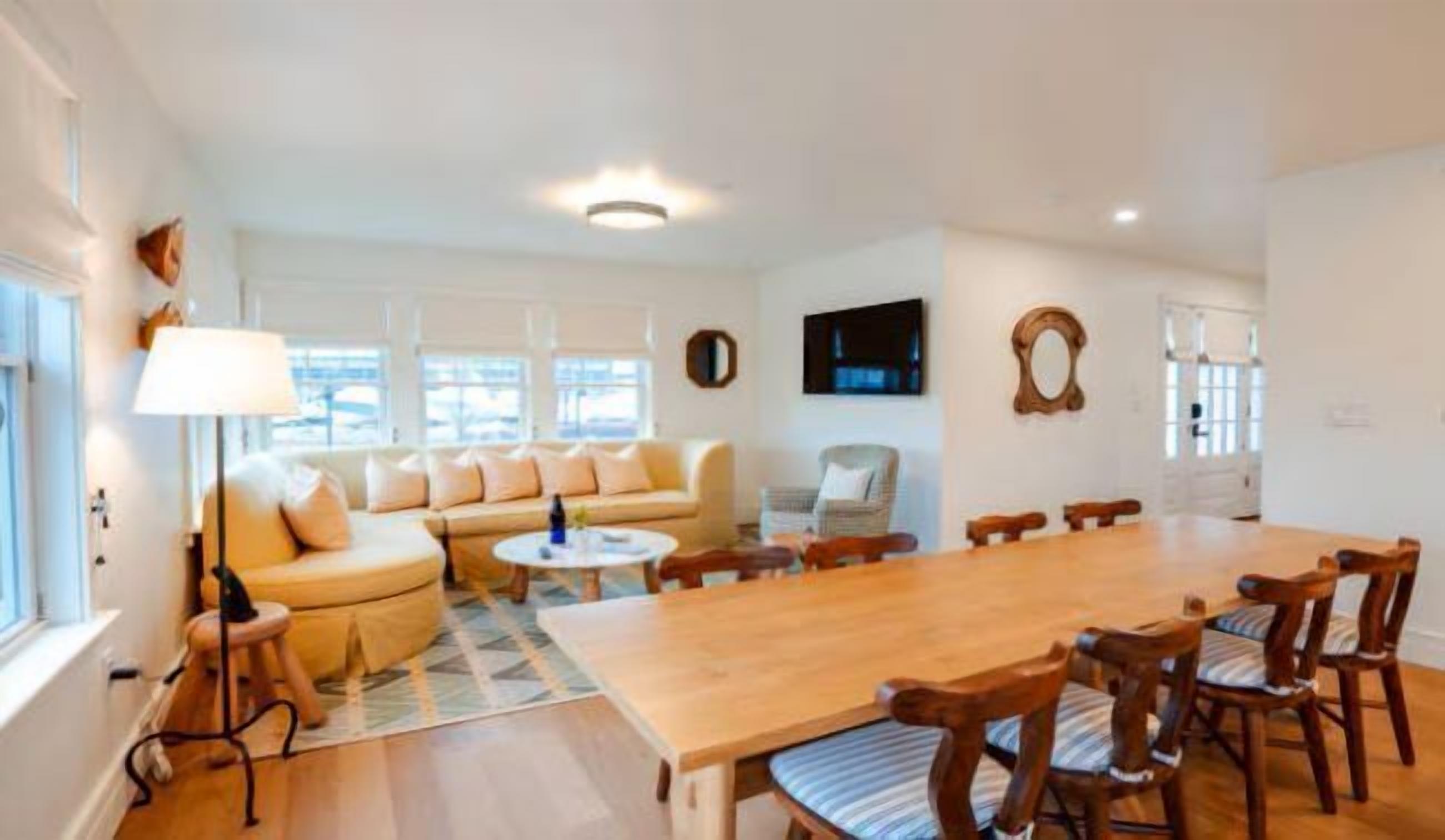 A spacious living room with a large wooden dining table, a sofa, and a TV mounted on the wall.