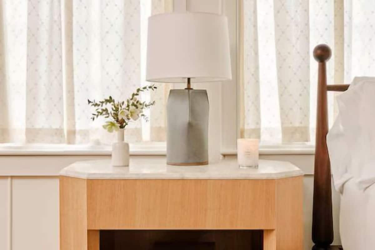 Une table de chevet bien rangée, avec une lampe, un petit vase de fleurs et une bougie.